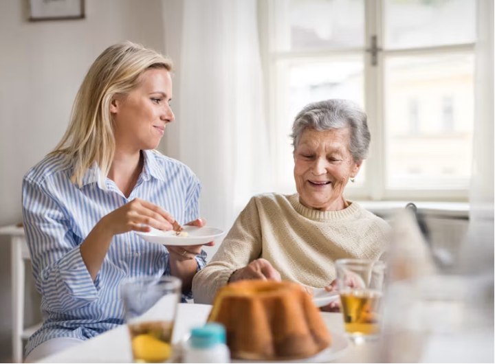 Jüngere Frau und Seniorin sitzen bei Kaffee und Kuchen am Tisch und unterhalten sich